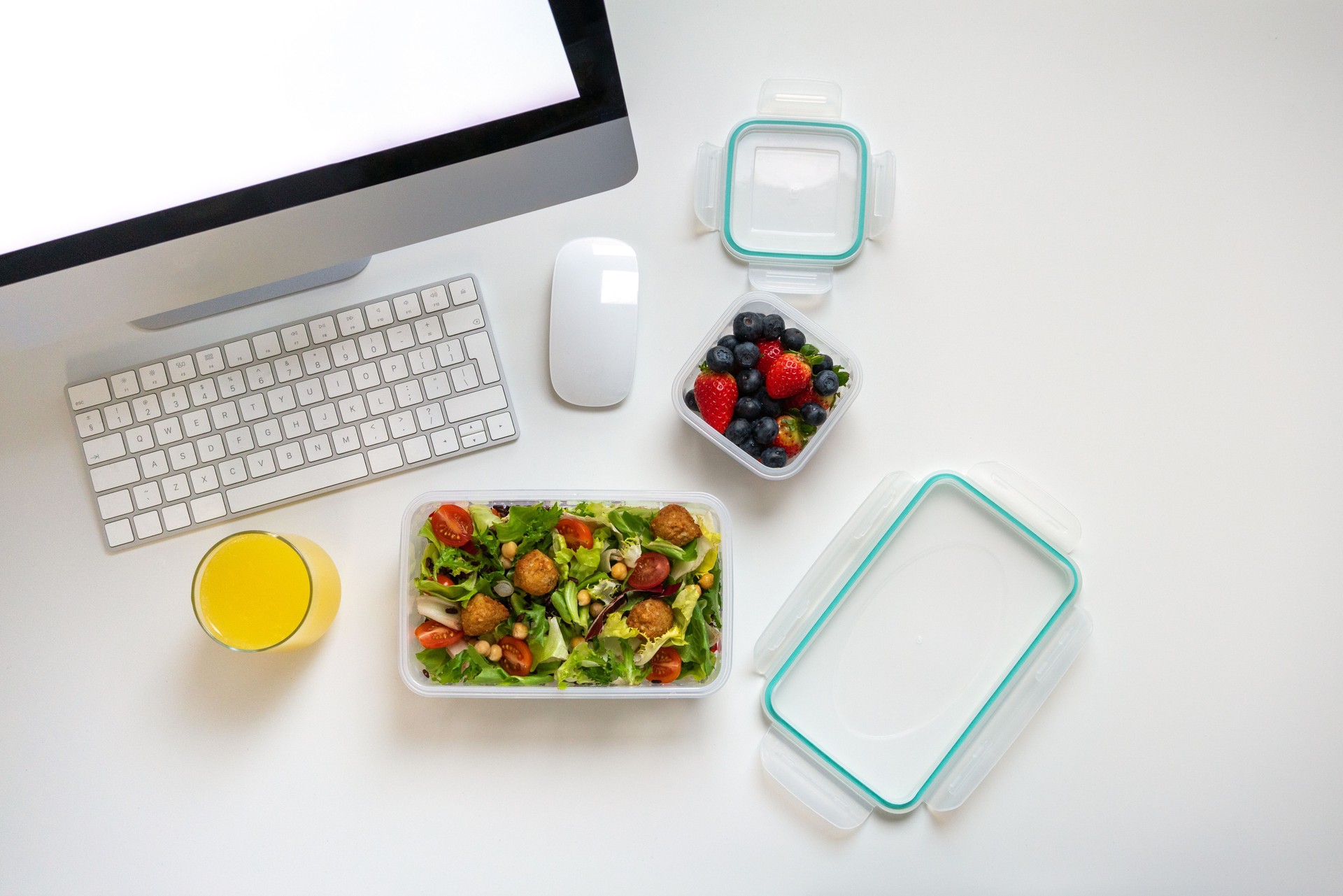 Reusable plastic boxes with salad and fresh berries at the work desk